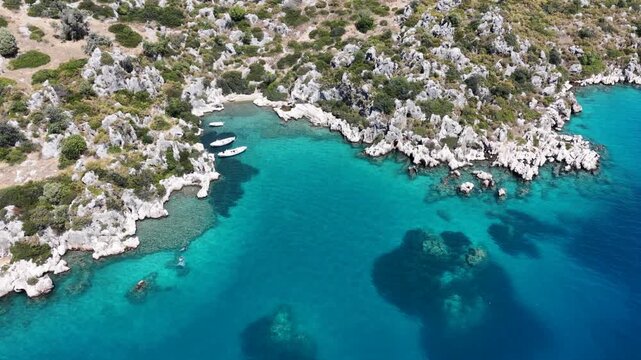Aerial top-down video of small white boats anchored in a hidden rocky cove with crystal clear turquoise water in Kekova, Turkey.