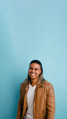 Fototapeta premium Cheerful latino man wearing a leather jacket, looking at camera and smiling with happiness in a studio setting