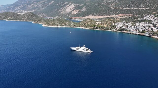 Aerial orbit shot around a luxury superyacht anchored in the deep blue waters of Kas, Turkey.