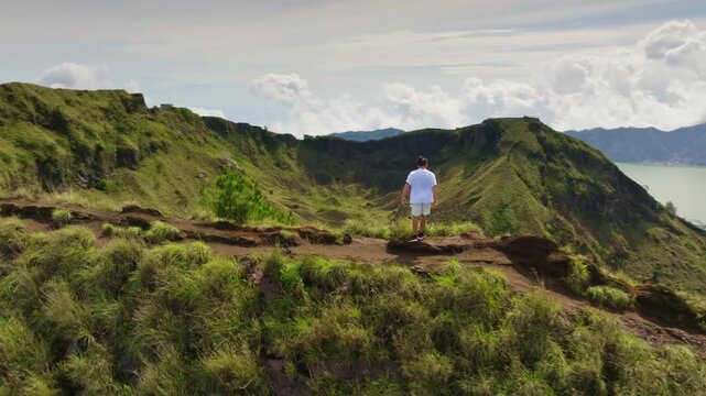 Man running on a scenic mountain trail, enjoying the panoramic view of the vast caldera, volcanic lake, and Mount Batur volcano under a cloudy sky in Bali, Indonesia. Active sports, outdoor activities
