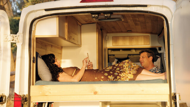 Mature couple relaxing on a bed inside a customized camper van, enjoying the van life freedom and travel adventure