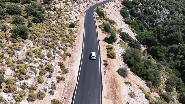 Aerial tracking shot of a white car driving along a newly paved winding mountain road.