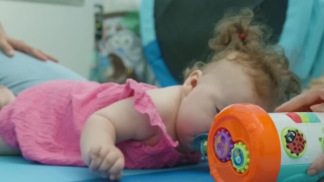 A baby girl lies on a play mat next to a colorful toy roller