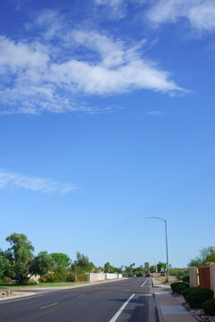 Quiet suburban asphalt street curves into the distance under an expansive blue sky filled with beautiful scattered monsoon white clouds, Phoenix, Arizona; copy space