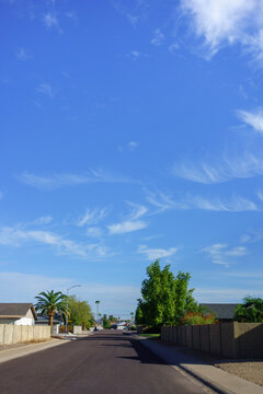 Sunday morning at quiet suburban street beneath a vast blue sky filled with wispy white monsoon clouds and lined with residential walls, Phoenix, Arizona; copy space