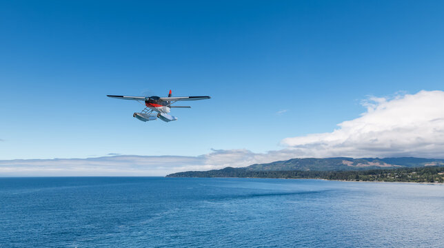 Floatplane Flying Over Ocean Near Coastal Mountains With Clear Sky and British Columbia Background