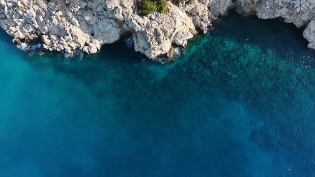 Aerial top-down static shot of a rugged rocky coastline meeting deep blue Mediterranean water.