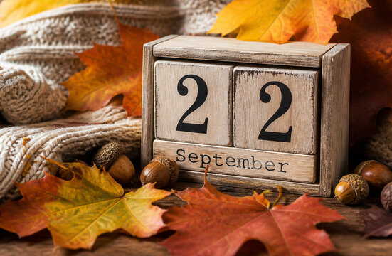 Wooden block calendar showing September 22 surrounded by colorful autumn maple leaves knitted scarf and acorns representing autumn equinox cozy fall season stock photo