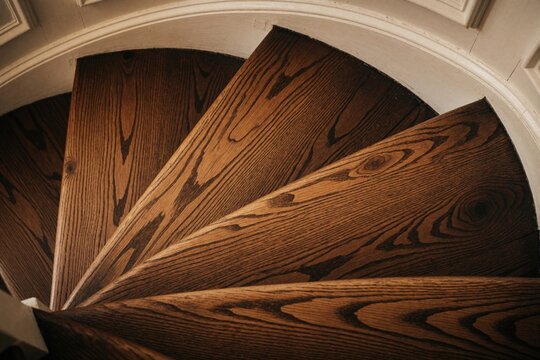 Closeup spiral wood stair treads, rich grain detail. Curved hardwood stpic indoors, classic architectural detail for home interior design. Elegant wooden staircase.