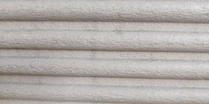 Close-up of a white plaster or concrete wall featuring parallel horizontal raised ridges, subtle rough texture, and soft neutral tones, suitable for architectural backgrounds and minimalist interiors.