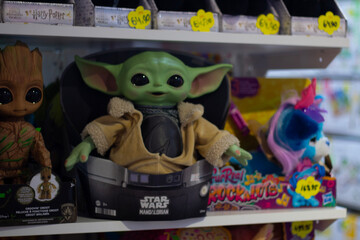 Fototapeta premium Horizontal photo. Grogu Yoda doll from Star Wars Mandalorian on toy store shelf with other toys. Green alien character action figure in packaging. Merchandise, pop culture, kids games, retail shopping