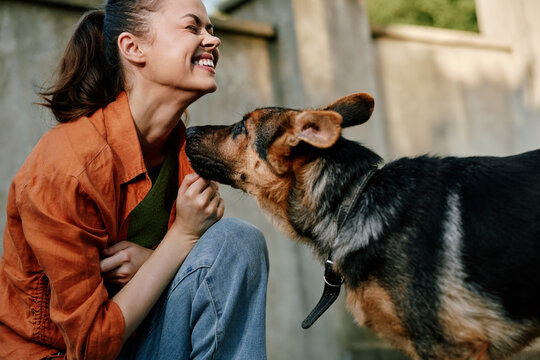 Happy woman laughing as a shepherd dog licks her face outdoors. Moment of joy, friendship, and love between human and pet. Concept of companionship and happy lifestyle with animals.