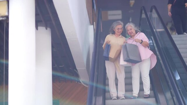 Happy Asian senior women friends enjoying shopping at mall, holding shopping bags and smiling together, active retirement lifestyle, consumer spending, friendship leisure activity and aging gracefully
