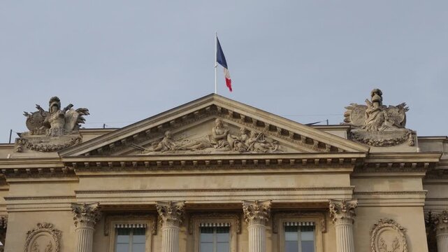 French tricolor flag flying over an ornate classical building with sculptures and columns in Paris