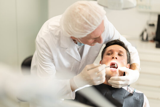 Man is sitting in armchair during dental diagnosis at dentist appointment. Senior man doctor conducts examination procedure, identifies problem areas and tests sensitivity of teeth
