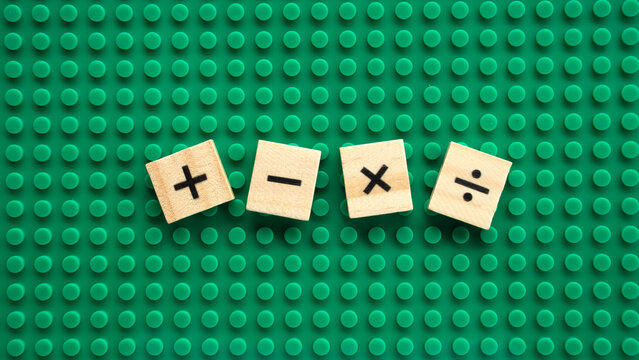 Square wooden tiles with math arithmetic symbols on green plastic building baseplate