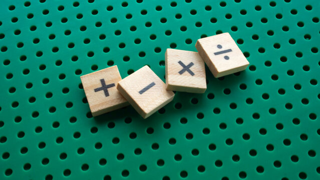 Wooden blocks with math operators plus minus multiply divide on green perforated surface