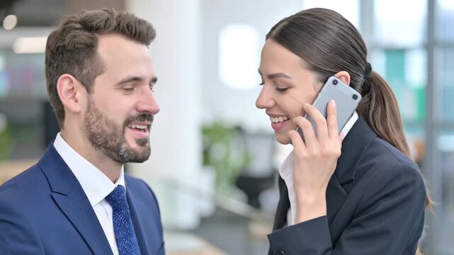 Businesswoman Talking on Smartphone while Consulting with Colleague in Office
