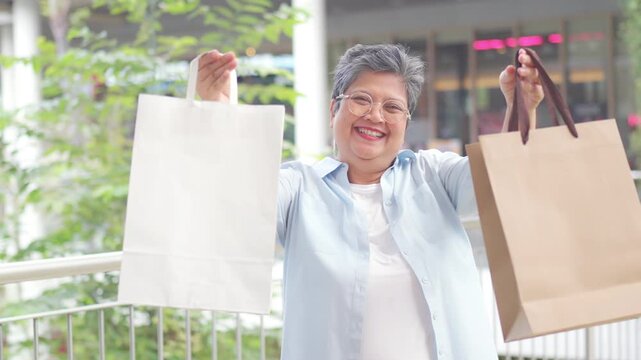 Happy Asian senior woman holding shopping bag at shopping mall, smiling after retail purchase, consumer spending, active retirement lifestyle, independent living, leisure activity and aging gracefully