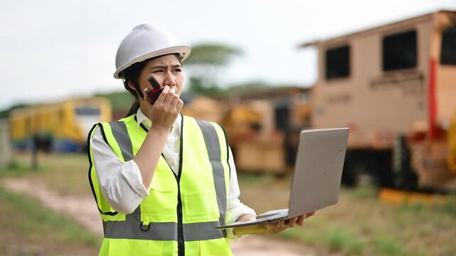 Female railway worker using walkie-talkie and laptop at train yard during daytime