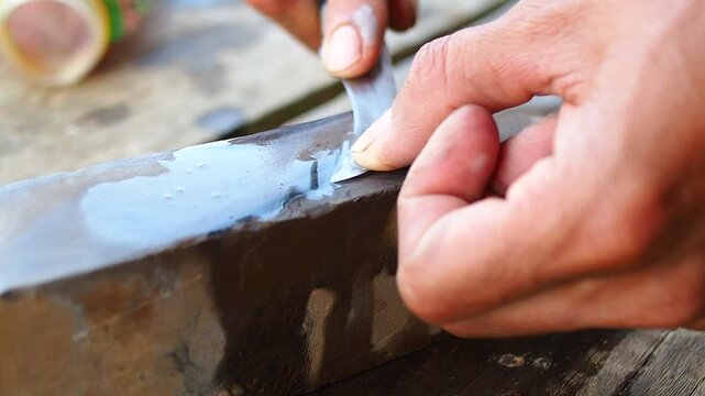 Close-up of Hands Sharpening a Small Curved Knife on a Wet Whetstone