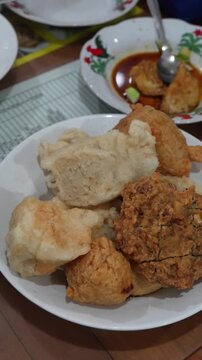Cinematic close-up of pempek Palembang with fried fish cake and ebi cracker. Served with brown cuko sauce and cucumber. Perfect for Indonesian street food content.