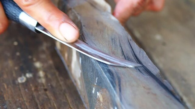 Close-up of hands sharpening a curved blade knife on a whetstone with water