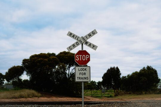 A rural railway crossing marked by a prominent crossbuck, stop sign and &ldquo;Look for Trains&rdquo; warning, set against a softly clouded sky and surrounded by trees and farmland, Sea Lake, Victoria, Australia