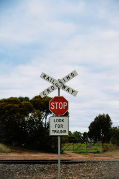A rural railway crossing marked by a prominent crossbuck, stop sign and &ldquo;Look for Trains&rdquo; warning, set against a softly clouded sky and surrounded by trees and farmland, Sea Lake, Victoria, Australia