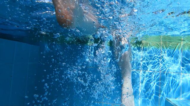 Slow motion underwater video of a girl dangles her feet in the pool water.