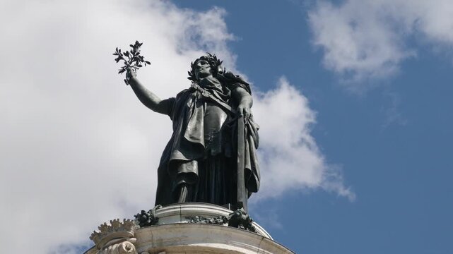 Marianne statue holding a branch, symbolizing liberty and Republic, against a blue sky in Paris