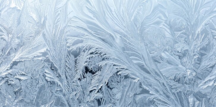 Intricate frost patterns on a glass window, featuring delicate fern-like ice crystals in shades of cool blue and white, creating a natural winter background texture