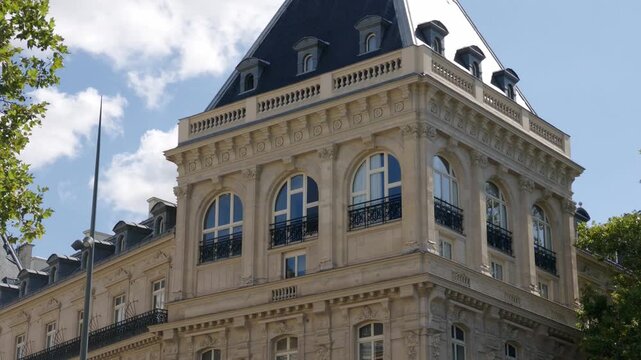 Ornate Haussmannian facade featuring arched windows and mansard roof against a summer sky