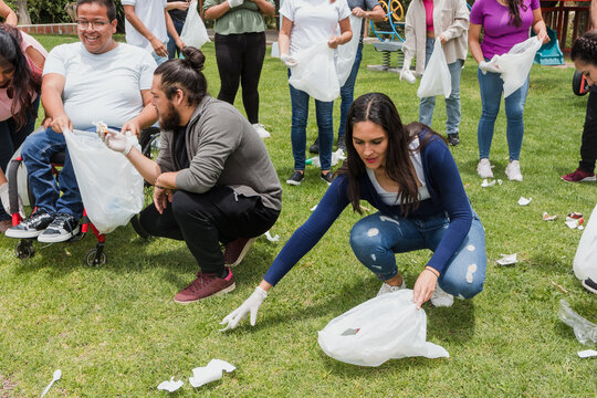 latina woman collecting trash in a public park in Mexico, Latin America. Group of multi age Hispanic volunteers cleaning up and collecting plastic in save the planet and ecology concept