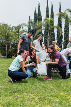 Group of diverse Latin people collecting trash in a public park in Mexico, Latin America. Group of multi age Hispanic volunteers cleaning up and collecting plastic in save the planet concept