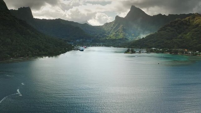Dramatic landscape of Moorea's Cook's Bay, lush green mountains, tranquil turquoise lagoon water and large cruise ship docked at tropical island, paradise travel destination. Aerial view drone shot
