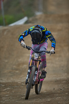 A downhill mountain bike racer catches full air off the final jump before the finish line, full-face helmet locked forward and body poised in perfect control mid-flight.