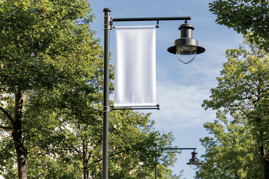 Blank white vertical banner hanging from a street lamp post with trees and blue sky