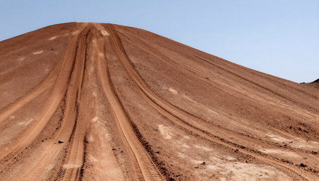 Dirt Track Ascending a Hill: A steep dirt hill marked with tire tracks leads upward under a clear blue sky, suggesting an off-road adventure or a path carved by vehicles.