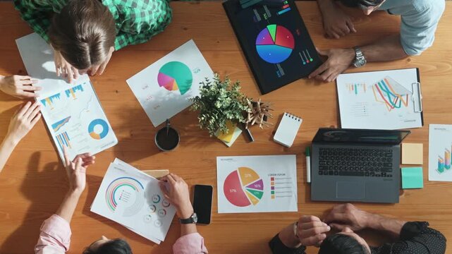 Top view of project manager using tablet to analyze data and financial chart while marketing team working together to brainstorm marketing campaign or planning strategy at meeting room. Convocation.