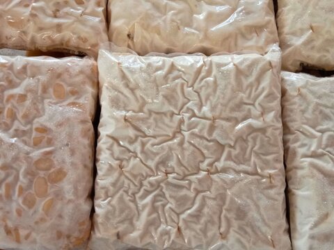 Piles of fresh raw tempeh blocks individually wrapped in plastic packaging