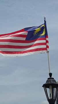 Malaysian national flag waving in the breeze next to a street lamp with Homo sapiens visiting the area