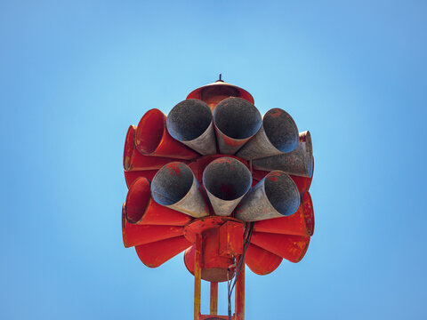 Close-up low angle view of a vintage red multi-horn civil defense tornado emergency warning siren against a clear blue sky. Ideal for articles on severe weather alerts, tornado warnings, civil defense