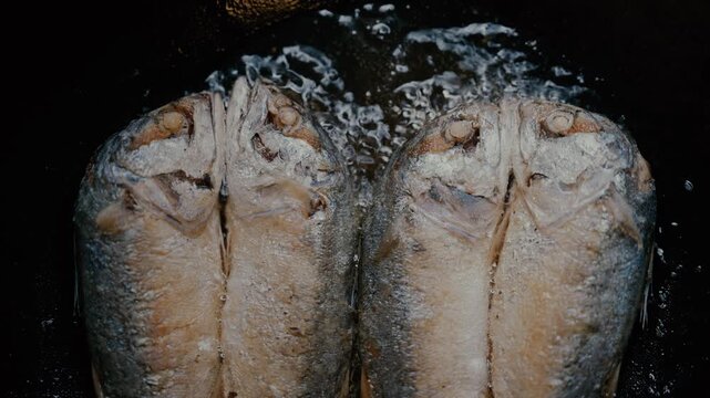 Close up of traditional short mackerel fish frying in hot bubbling oil in pan.
