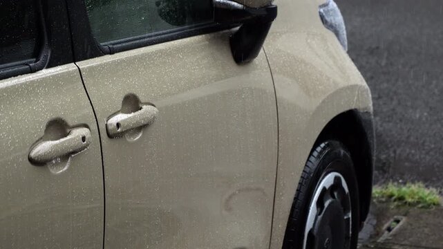 Raindrops falling on the exterior of a beige car parked outdoors during rain