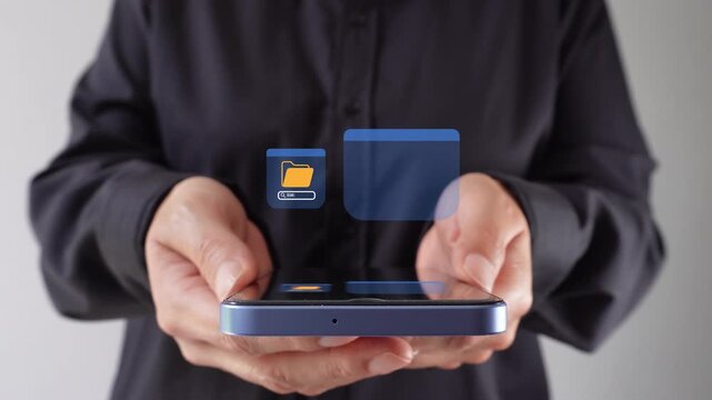 A person is holding a smartphone displaying folder management icons. The focus is on the hands and the device.