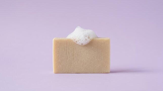Single bar of natural soap with white foam bubbles on top, isolated on a solid light purple background