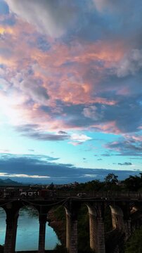 Vertical Video: Ancient stone arch bridge over the Hongshui River with a white car crossing under dramatic sunset clouds