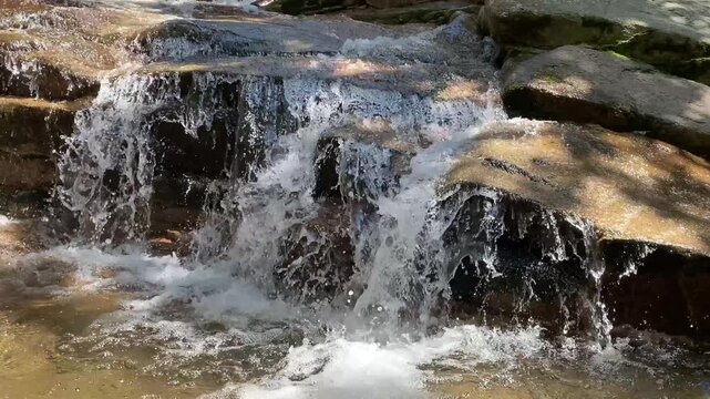 Clear mountain stream water splashing down flat rocks under sunlight
