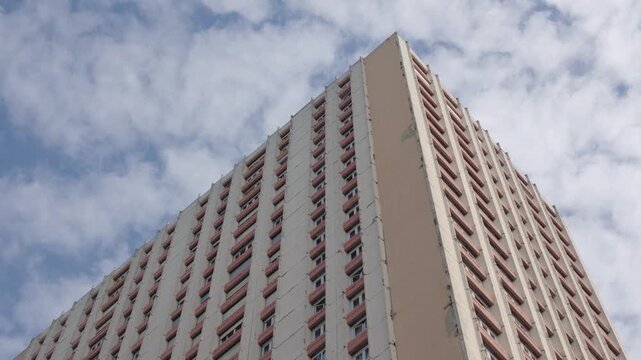 Brutalist architecture of a tall housing tower reaching the blue sky with clouds